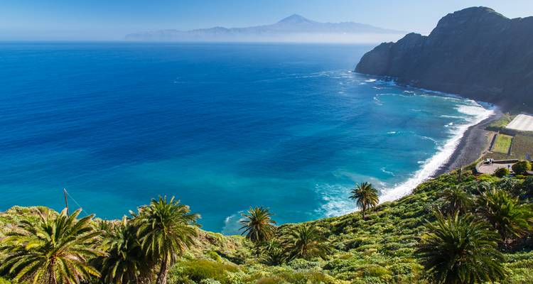 Stunning high cliff coastline with emerald water and distant hazy mountain under clear blue sky.