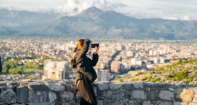 Reisender fotografiert panoramische Stadt- und Berglandschaft von Steinfortificationsmauern bei Sonnenuntergangslicht