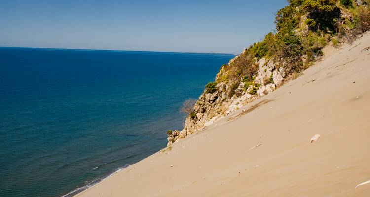 Steile Sanddüne, die zu tiefblauem Meer entlang einer rauen Küstenlinie an einem klaren Tag abfällt