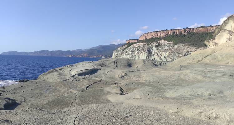 Plateau côtier rocheux dominant la Méditerranée bleu profond avec des falaises escarpées et des montagnes lointaines sous un ciel dégagé.