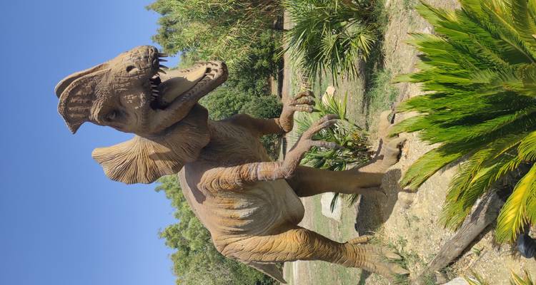 Statue de dinosaure à taille réelle rugissant dans un parc extérieur par une belle journée ensoleillée.