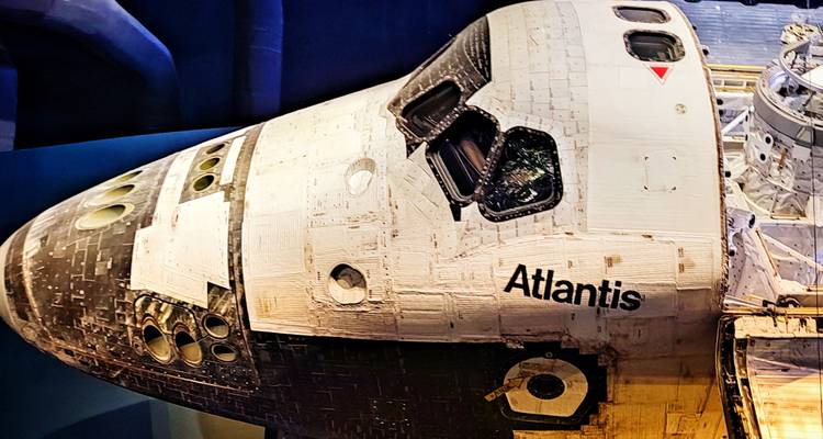 Vue rapprochée de l'orbiteur de la navette spatiale Atlantis exposé dans une exposition muséale avec des tuiles thermiques détaillées visibles.