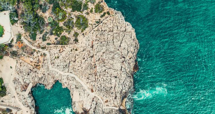 Vue aérienne d'une péninsule rocheuse et accidentée entourée d'une mer turquoise éclatante avec des vagues déferlantes.