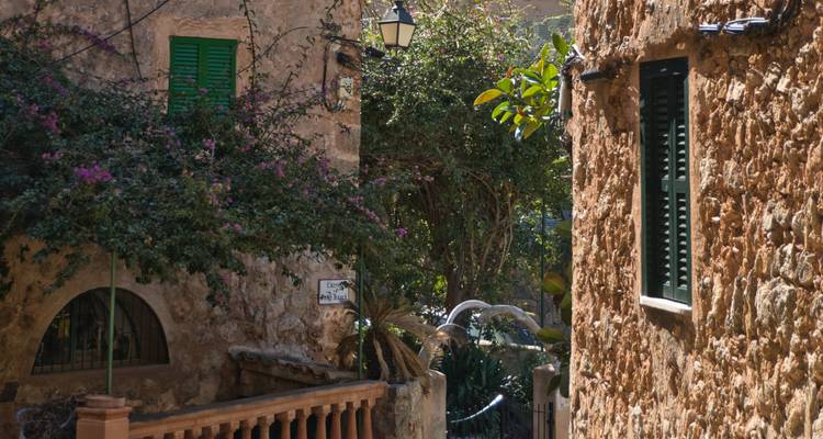 Ruelle de pierre tranquille avec du bougainvillier luxuriant grimpant sur les façades et des volets verts traditionnels.