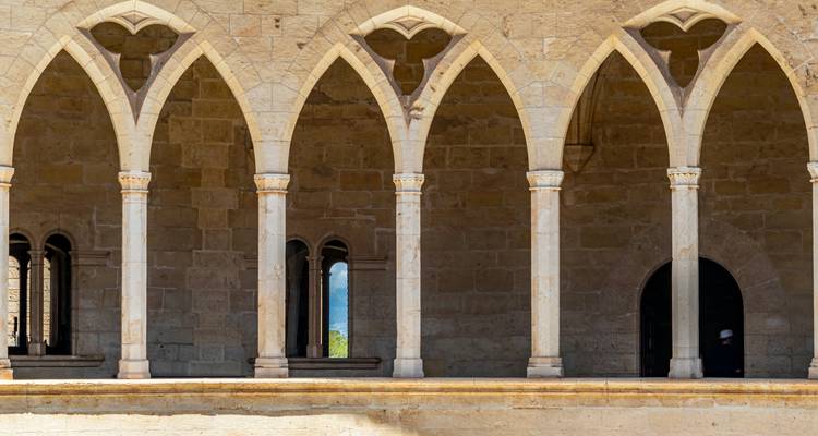 Série d'arcs gothiques pointus dans un cloître en pierre claire avec des portes ombragées.