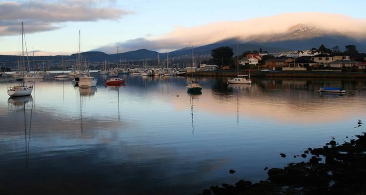 Marina paisible avec des voiliers se reflétant sur une eau calme et des montagnes couvertes de brume en arrière-plan à l'aube.