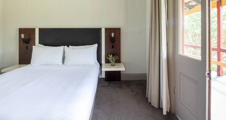 Lichte, minimalistisch hotelkamer met tweepersoonsbed, witte lakens en balkondeur met natuurlijk licht