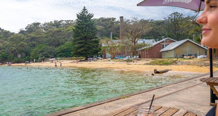 Tafel in een strandcafé met uitzicht op een rustige zandige baai omgeven door eucalyptusbos en rustieke gebouwen