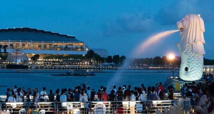 Multitud nocturna viendo la fuente Merlion brotando agua a través de Marina Bay