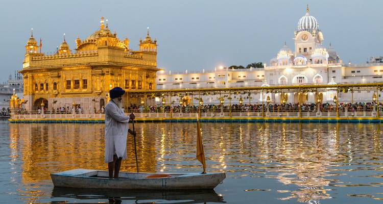 A lone devotee rows on the shimmering pool before the illuminated Golden Temple at dusk.
