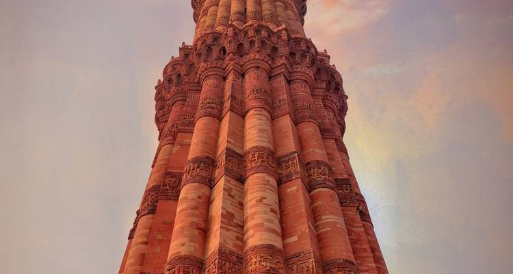 Upward view of the intricately carved red-sandstone Qutub Minar bathed in soft sunset light.