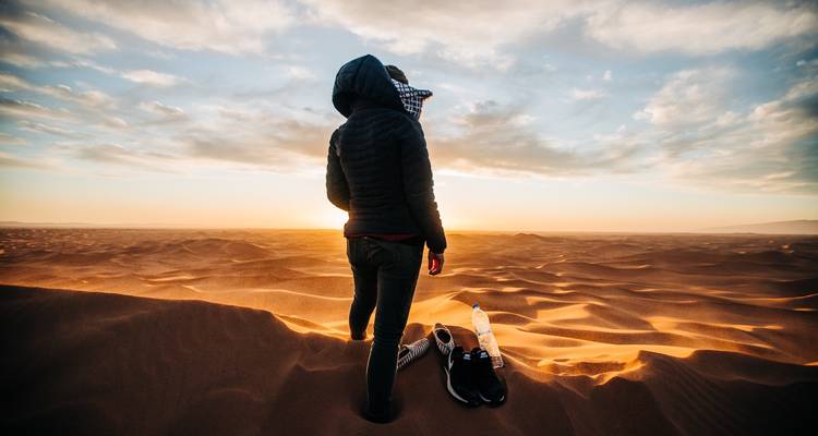 Reiziger staat blootsvoets bovenop uitgestrekte golvende duinen terwijl de zon ondergaat over de Sahara.