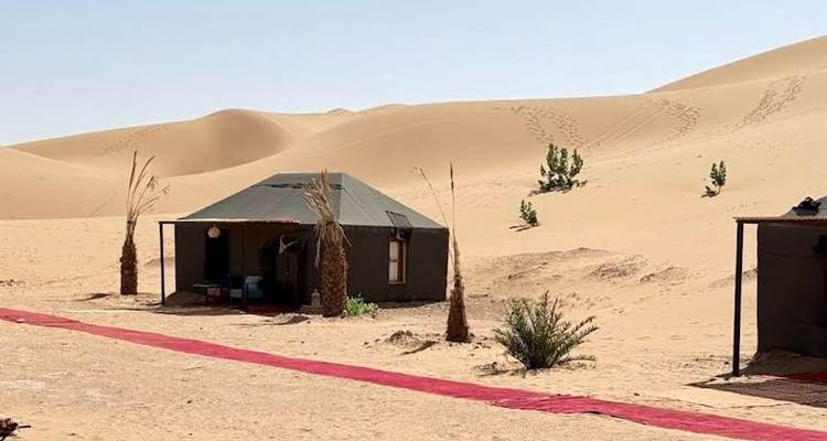 Een enkele canvas tent staat op open woestijnzand onder een heldere blauwe hemel.