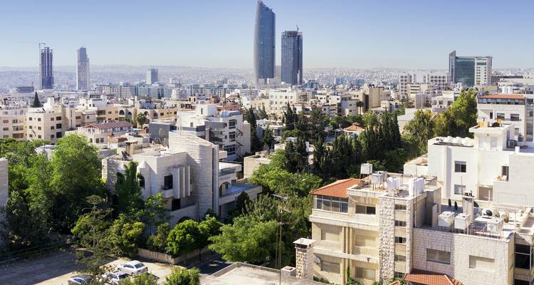Modern residential and commercial buildings with evergreen trees in Amman under clear skies