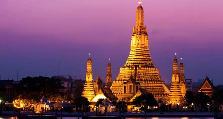 Le temple Wat Arun illuminé en violet crépusculaire sur les rives du fleuve Chao Phraya.