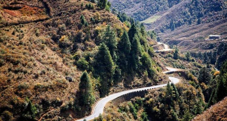 Winding mountain road weaving through forested, rugged Bhutanese hills.
