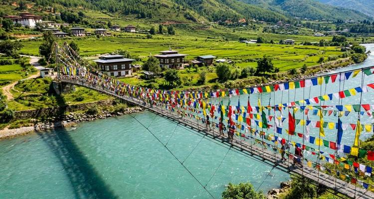 Suspension footbridge draped with colorful prayer flags crossing turquoise river in Punakha.