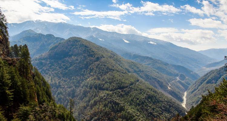 Layered mountain ridges and forested valleys under a bright sky in Bhutan.