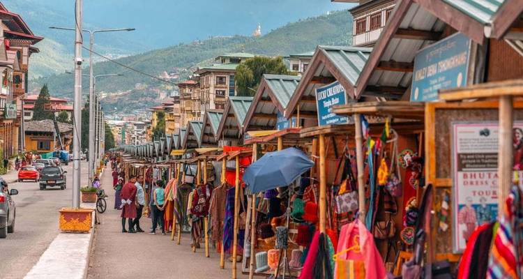 Open-air craft market stalls lined along a Bhutanese town street with locals browsing.