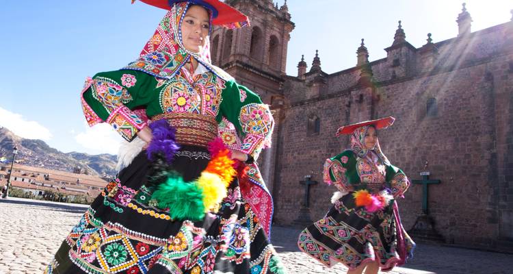 Two Peruvian dancers in brightly embroidered traditional costumes performing in a cobblestone square beside an old stone church.
