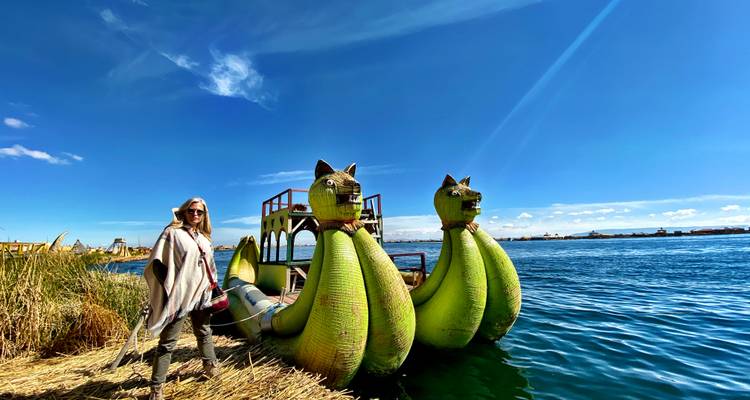 Traveller stands beside whimsical green reed boats shaped like cats on the blue waters of Lake Titicaca.