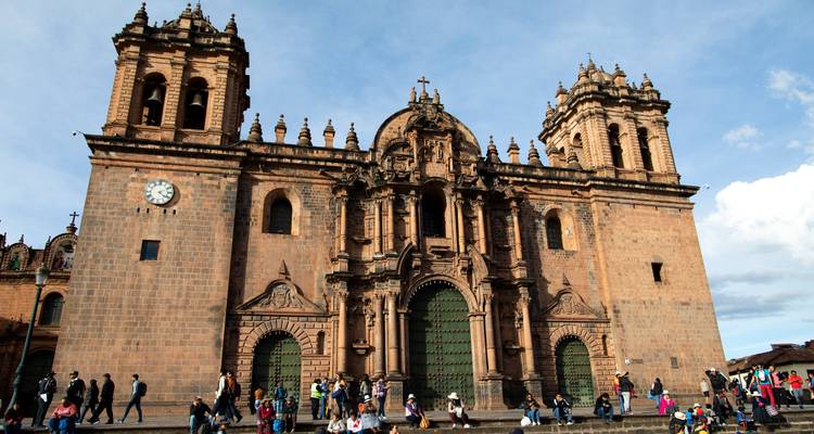 Grand stone façade of Cusco Cathedral towers over crowds gathered on the steps of Plaza de Armas.