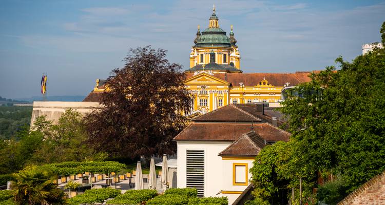 Baroque Melk Abbey glowing in morning sun above terraced gardens and lush greenery.