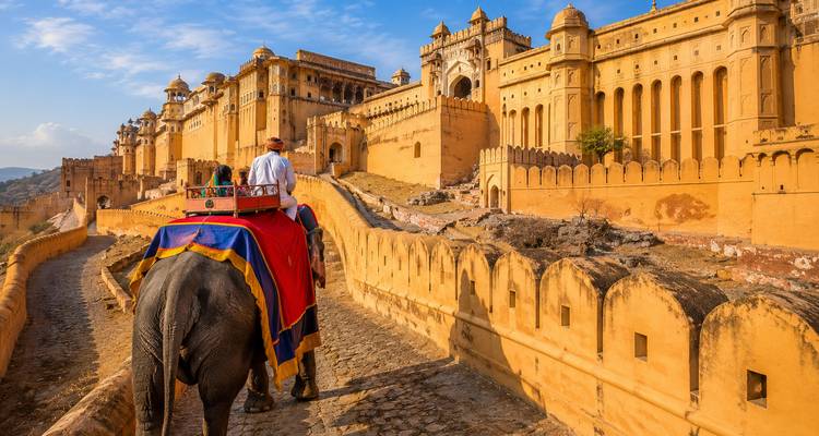 Touristen reiten auf einem Elefanten die steinernen Wälle hinauf in Richtung der goldenen Mauern des Amber Fort in Jaipur.