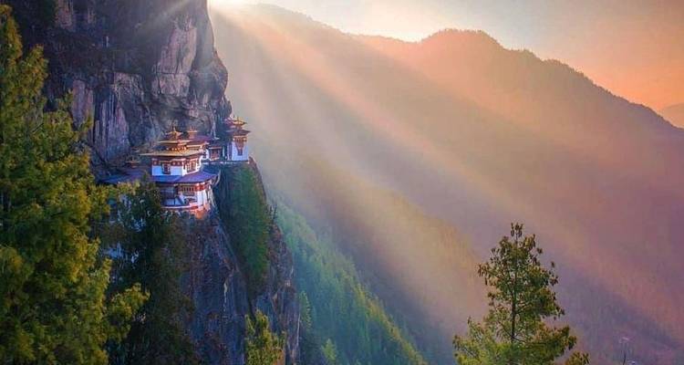 The famous Tiger’s Nest monastery perched dramatically on a cliff with golden morning rays streaming across a forested mountain valley.
