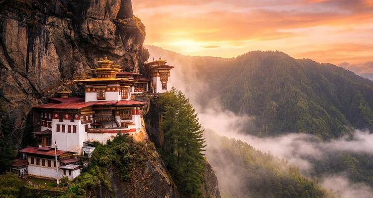 Tiger’s Nest monastery glowing at sunset above mist-filled forested cliffs.