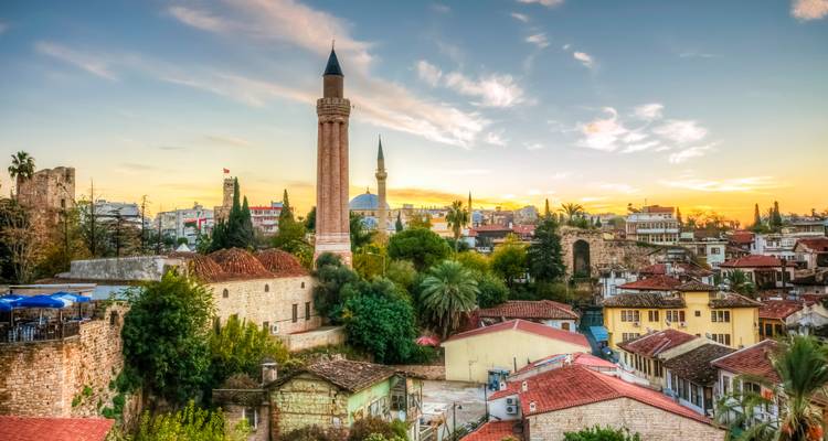 La lumière du coucher de soleil baigne l'horizon d'Antalya avec le minaret historique Yivli, les palmiers et les nuages aux teintes pastel.