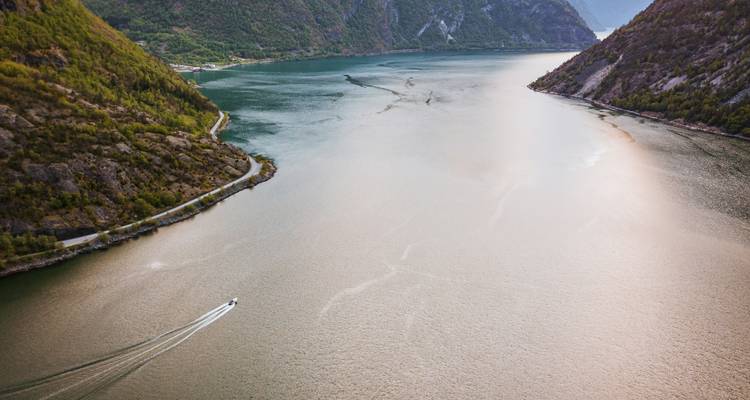 Vue aérienne d'un long fjord étroit avec un petit bateau rapide laissant un sillage au milieu de falaises imposantes.