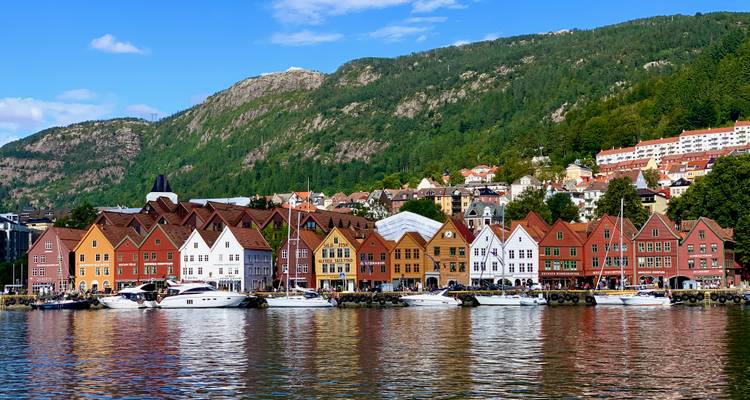 Les entrepôts colorés en bois de Bryggen bordent le front de mer de Bergen avec des collines boisées en arrière-plan.
