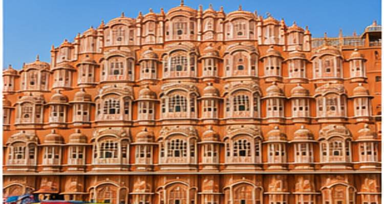 De ingewikkelde roze gevel van Hawa Mahal rijst op tegen een helder blauwe lucht, met rijen van tralievensters en architectuur uit het Mughal-tijdperk.