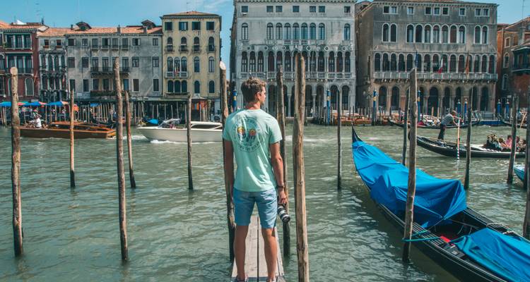 Un homme avec un appareil photo se tient sur des poteaux à côté du Grand Canal et observe les façades vénitiennes.