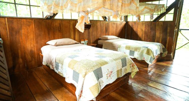 Chambre lumineuse avec deux lits simples garnis de courtepointes patchwork et de moustiquaires en mousseline
