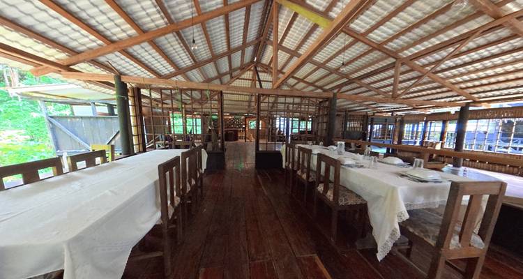 Salle à manger en plein air avec structure en bois et tables longues dressées pour les clients dans un lodge de jungle