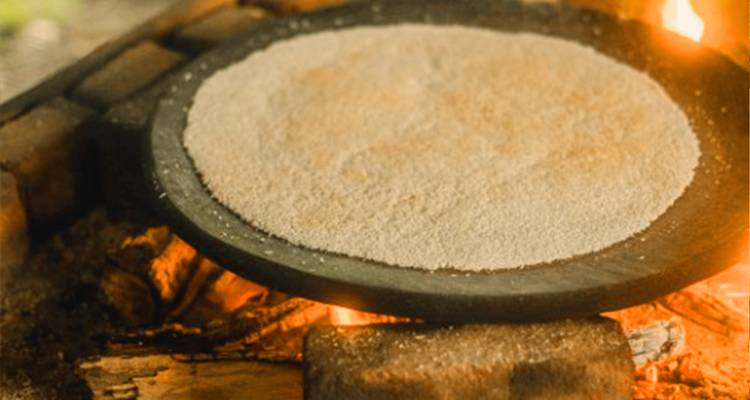 Gros plan sur la cuisson du pain plat traditionnel de manioc sur une plaque d'argile au-dessus d'un feu ouvert