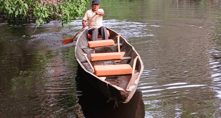 Un homme pagayant dans un étroit canoë en bois à travers les eaux calmes de la jungle
