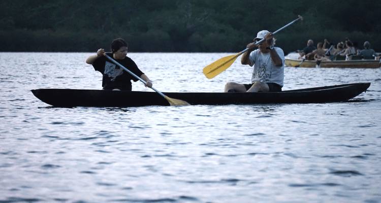 Paire de pagayeurs dans un canoë élancé en silhouette sur un large lac au crépuscule, autres embarcations en arrière-plan