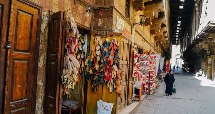 Callejón del mercado tradicional en El Cairo lleno de coloridas chancletas y textiles mientras los locales pasan por ahí.