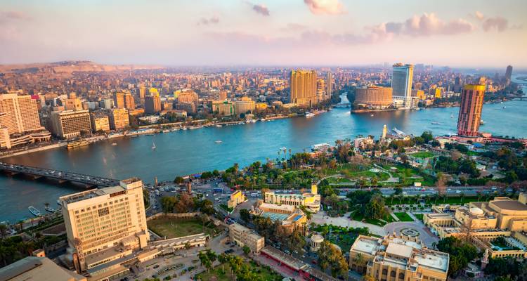 Vista aérea elevada del centro de El Cairo y el Nilo sinuoso al atardecer con las cálidas luces de la ciudad comenzando a brillar.