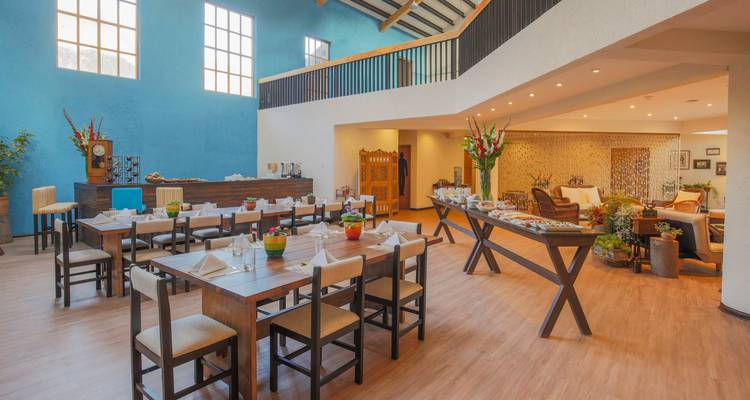 Bright, modern hotel dining room set with tables and a continental buffet beneath high skylights.