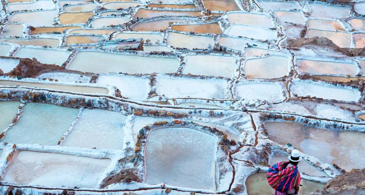 A traditionally dressed worker walks along the geometric salt terraces of Maras shimmering in pastel hues.