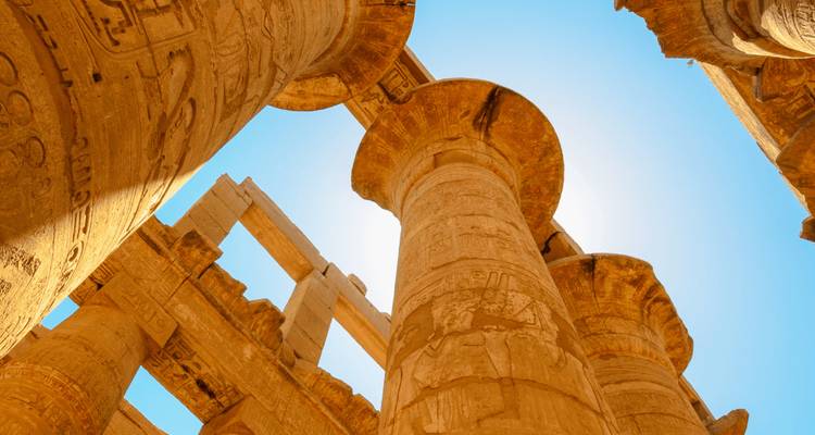 Vue ascendante des colonnes de grès colossales du Temple de Karnak brillant contre un ciel bleu clair.