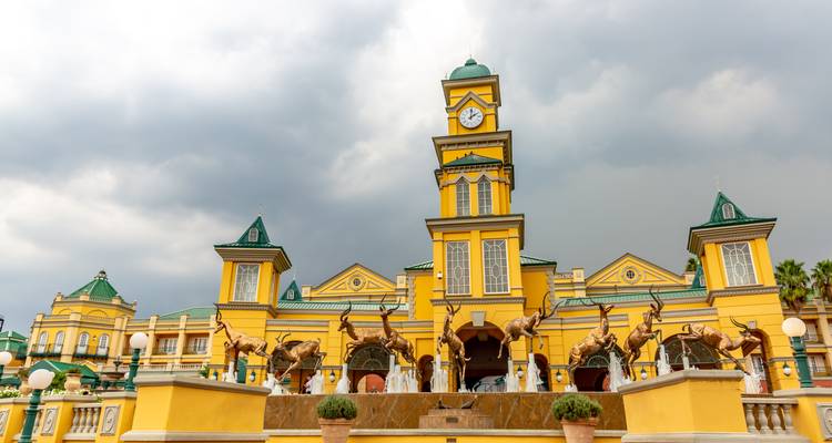 Fachada de la torre del reloj amarilla con esculturas de antílopes de bronce en frente de nubes de tormenta dramáticas.