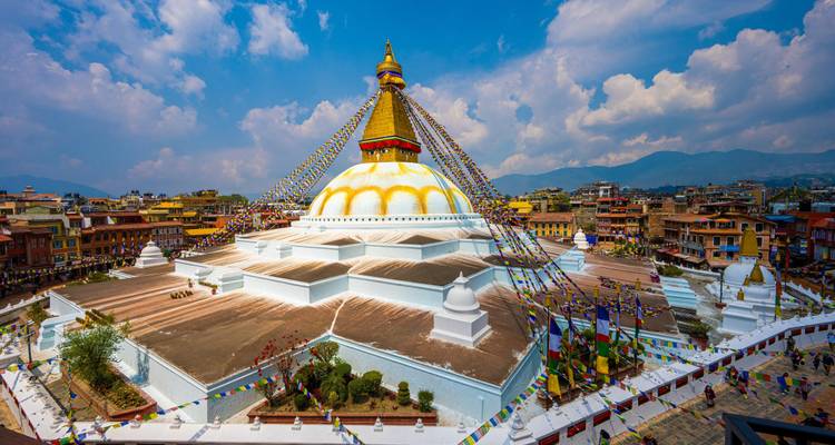 Foto gran angular vibrante de la estupa de Boudhanath con sus pisos blanco brillante y banderas de oración bajo un cielo dramático.