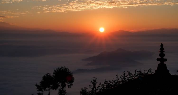 Un amanecer espectacular sobre un mar de nubes con siluetas de colinas lejanas y la punta de una pagoda en primer plano.
