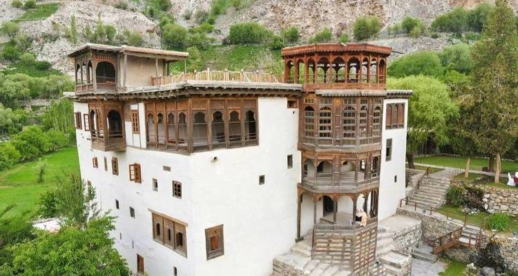 Le Palais de Khaplu aux fenêtres en bois historiques s'élève au-dessus des terrasses verdoyantes et de la versant rocheux.