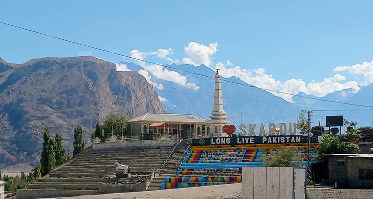 Les marches colorées « J'❤️ aime Skardu » et l'obélisque se dressent sur fond de montagnes escarpées et de ciel bleu.